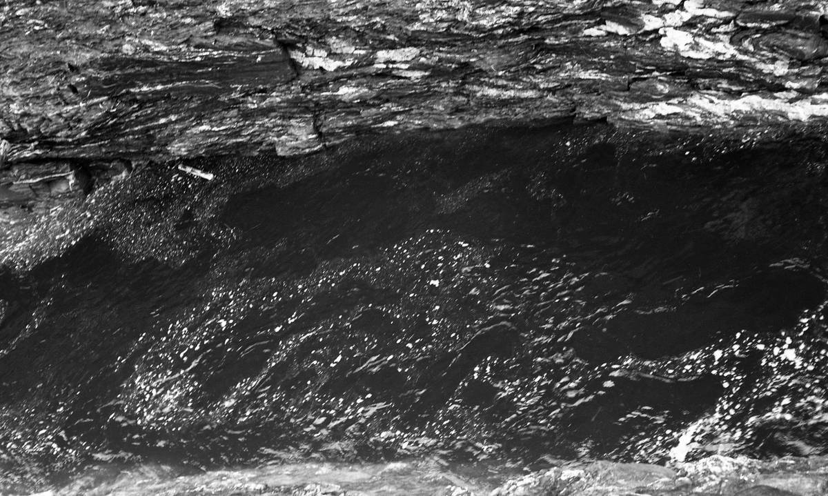 Noe av Kamfossen i Vinstravassdraget i Midt-Gudbrandsdalen, fotografert fra en bergskrent ned mot elveløpet, som renner i ei kløft i fjellet, på dette fotografiet renner fra venstre mot høyre. Kamfossen ligger der Vinstra renner ut av sjøen Olstappen, i Skåbu i Nord-Fron kommune. Fossen har et samlet fall på drøyt 40 meter, riktignok fordelt over flere terskler. Det er åpenbart at det var komplisert å drive tømmerfløting på en elvestrekning som denne. Når tømmeret satte seg fast her var det vanskelig og farefullt for mannskapene å ta seg ned for å løsne det. Olstappen ble regulert som magasin for kraftproduksjon i perioden 1953-55. Dette fotografiet er tatt cirka ti år seinere.