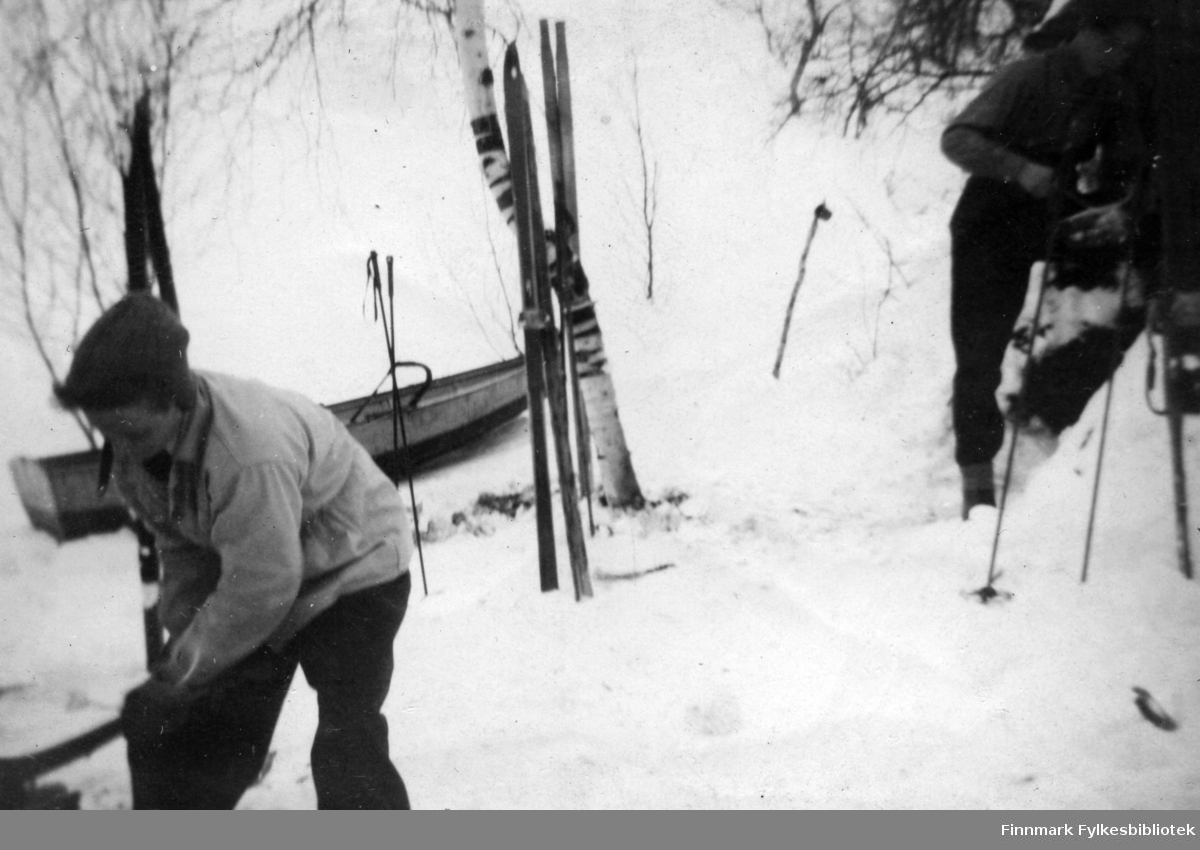 Harald Kjellmo, og Einar Isaksen utenfor gammen i Gokkmokka. Det står oppstilt ski i snøen. En båt, eller kjelke ses i bakgrunnen