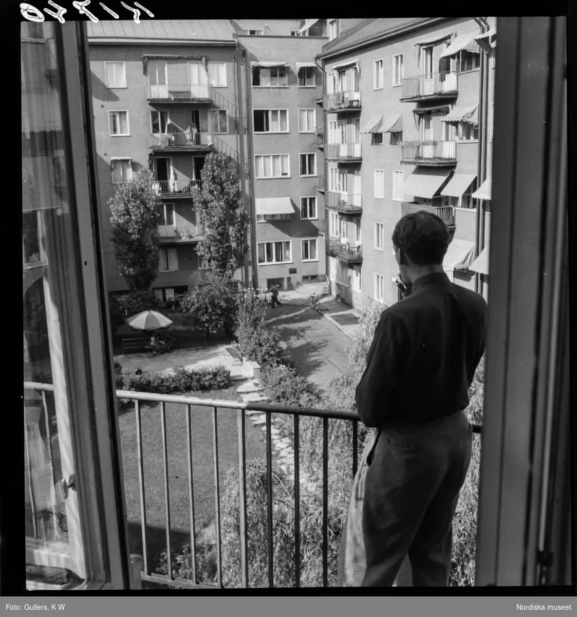 507 B Ultuna. En man står på en balkong och blickar ut över en innergård.