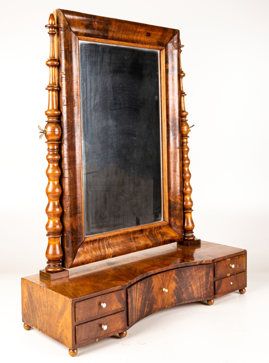 Byråspegel, (lådspegel) av rotmahogny. Med en större och fyra mindre lådor. Svarvade ståndare för spegelns upphängning.
