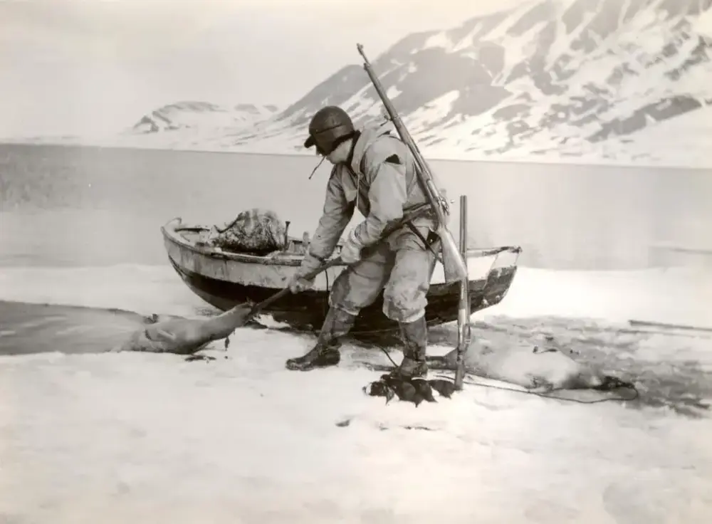 Mann med drept sel. Robåt, fjord og fjell i bakgrunnen.