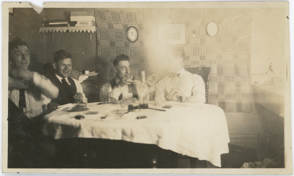 Fire unge menn har innvielsesfest for ny leilighet. De spiller kort og drikker, med snapsglass på bordet.