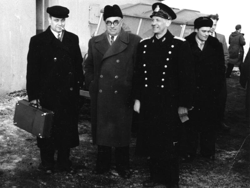 Svart/hvitt-bilde av to menn i dress og hatt, sammen med sysselmannen i uniform.
