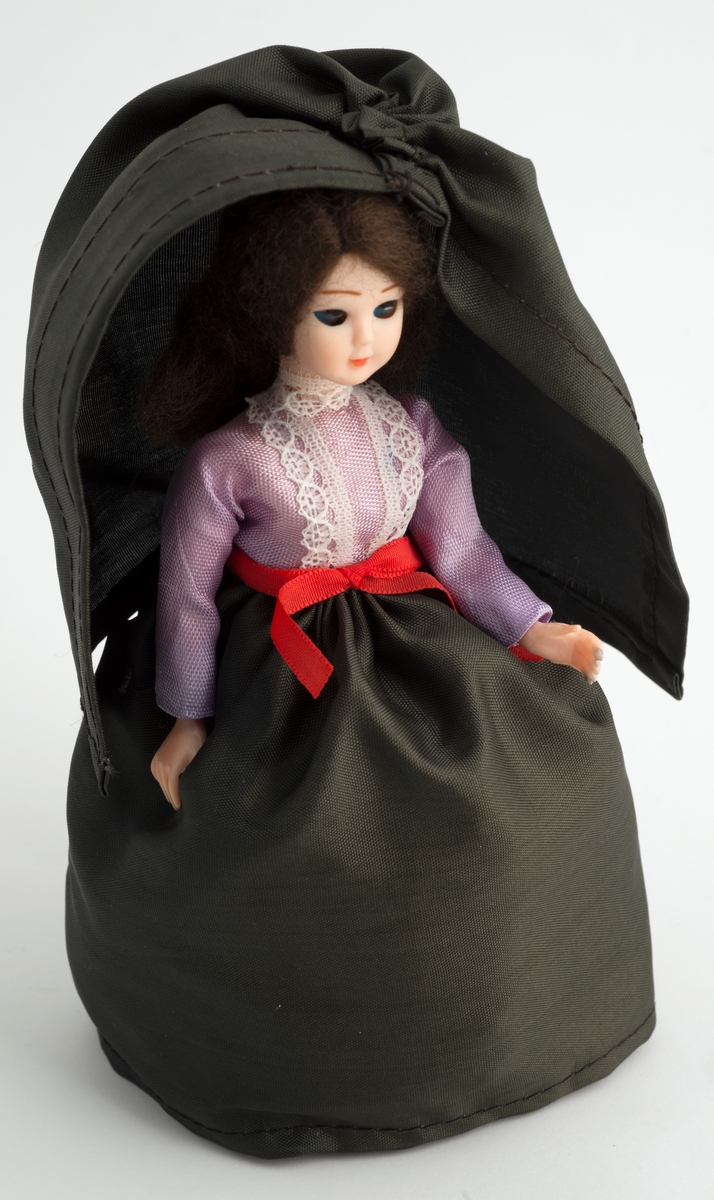 Kvinnefigur i svart kjole og svart cape.