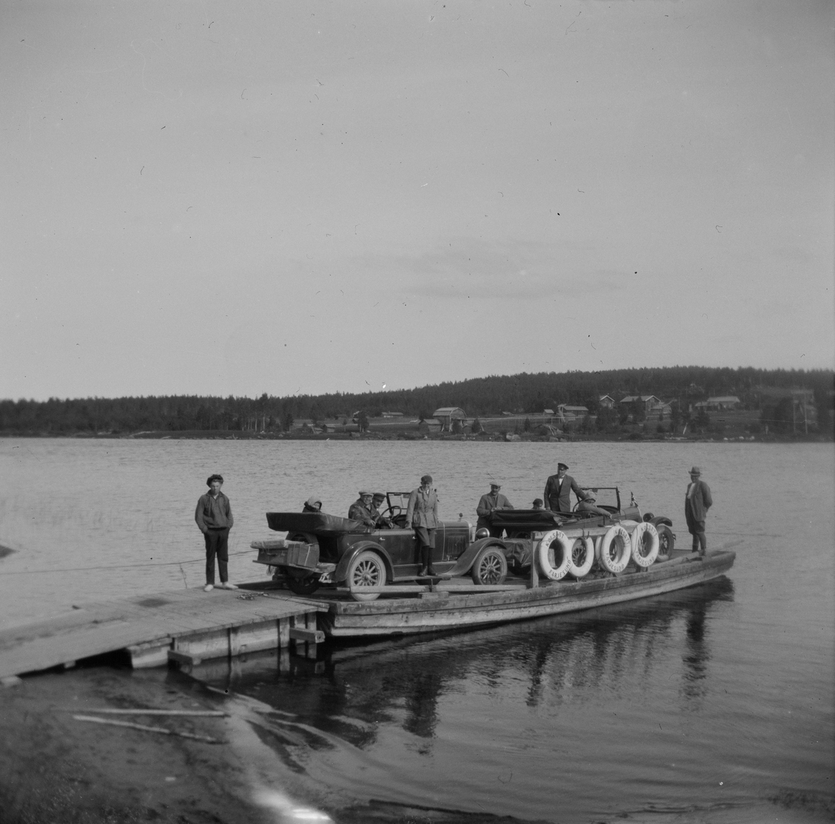 To biler og passasjerer på en lekter ved ei brygge