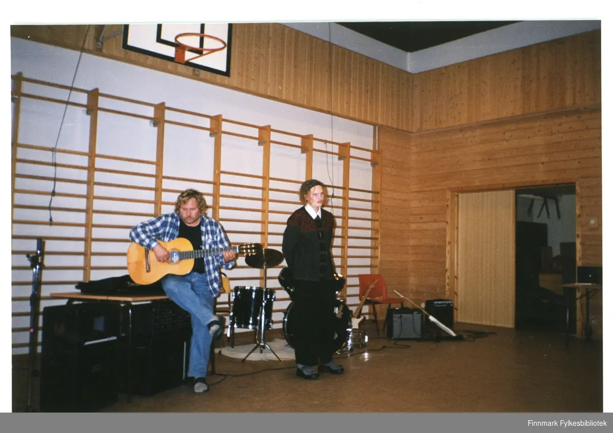 Ukjent (på gitar) og Annbjørg Dørmænen spiller gitar og synger på skolekonsert i gymsalen.