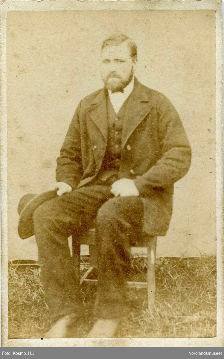 Portrett av en mann med skjegg, som sitter på en stol foran et oppspent lerret ute, med hatt i handen.