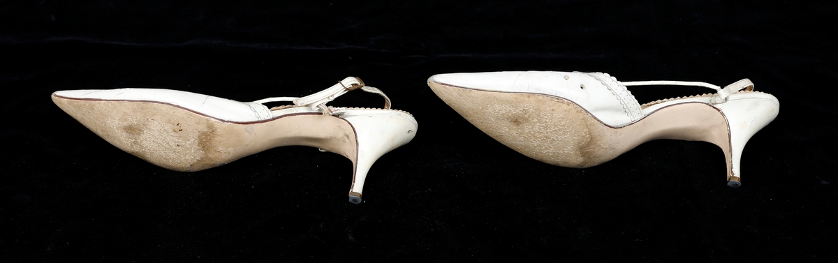 Et par hvite selskapssko til kvinne. Spiss tå, høye hæler. Metalltupp på hælen. Sålen på venstre sko er løs.