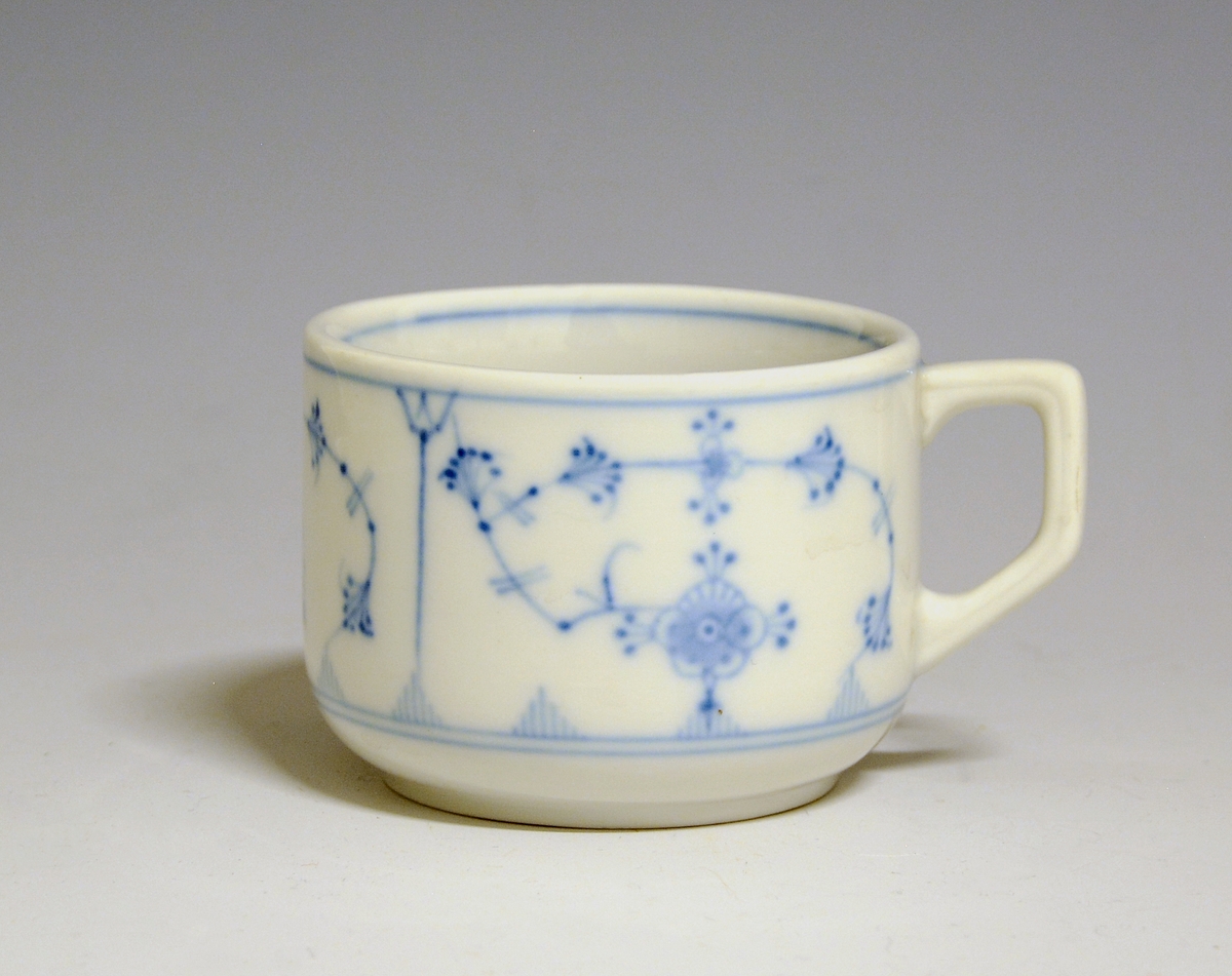 Kaffekopp med tykt gods av porselen med hvit glasur. Kantet hank. Dekorert med stråmønster i blått. Håndmalt: "Grand Hotel Drammen". 
Uten fabrikkmerke. 
Prøve?