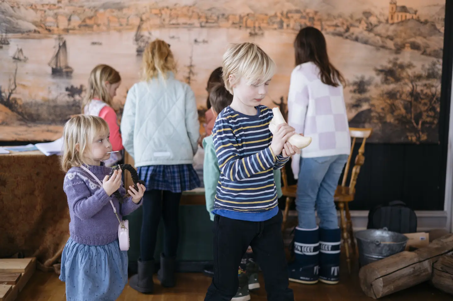 Flere barn på bildet og forrest en gutt som holder i en hvit hvaltann. Ei lita jente kikker nysgjerrig på.