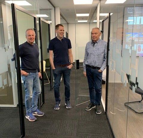 Tre menn stående i kontorgang