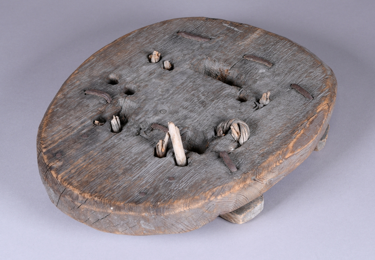 Hestetruge av tre. Oval plate av furu, med to tverrspiler på undersiden. Spilene er festet med kramper fra oversiden av platen. Platen har hatt reimer av vidje, men bare rester er igjen av dette.