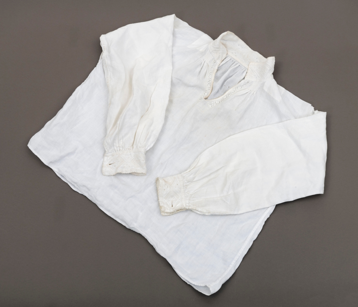 Bunadsskjorte med rik broderidekor i halslinning og ermlinning. Skade (slitasjehull) på venstre skulder.