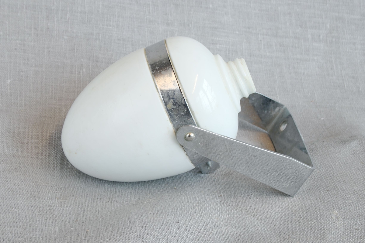 Oval beholder i hvitt glass med gjenger for skrukork øvert, samt metallbøyle for fastmontering. Ubestemmelig materiale. Uvisst bruksområde. Beholderen inneholder litt hvitt pulver.