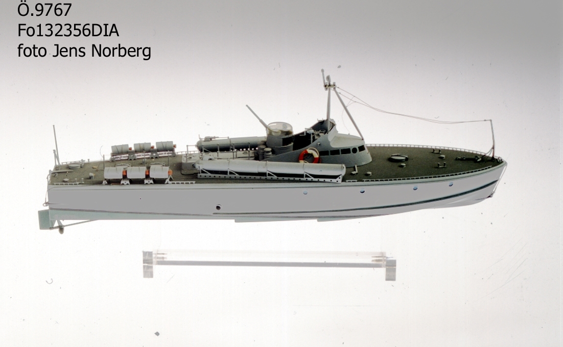 Modell av torpedbåt (motortorpedbåt), typ " T 15." Av trä med brygga, torpedtuber, sjunkbomber, kanon och övrig utrustning av metall. Skrovet ljust grått över vattenlinjen däcket grönt, däcksutrustning ljust grå, svart vattenlinje, undervattenskroppen grön. Skala 1:50.
Längd:  37 cm Bredd: 9  cm (framför bryggan).