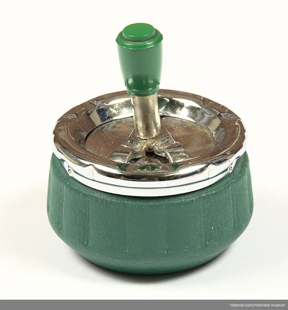 Cylindriskt formad grönmålad plåtburk med lock i förkromad plåt. Locket har en roterande mekanism som aktiveras genom ett tryck på en knapp klädd i grön hårdplast.