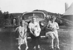 Fire jenter med en baby, fotografert på et gårdstun foran en