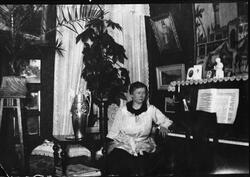 En kvinne sitter ved et piano. Interiørbilde fra en stue.