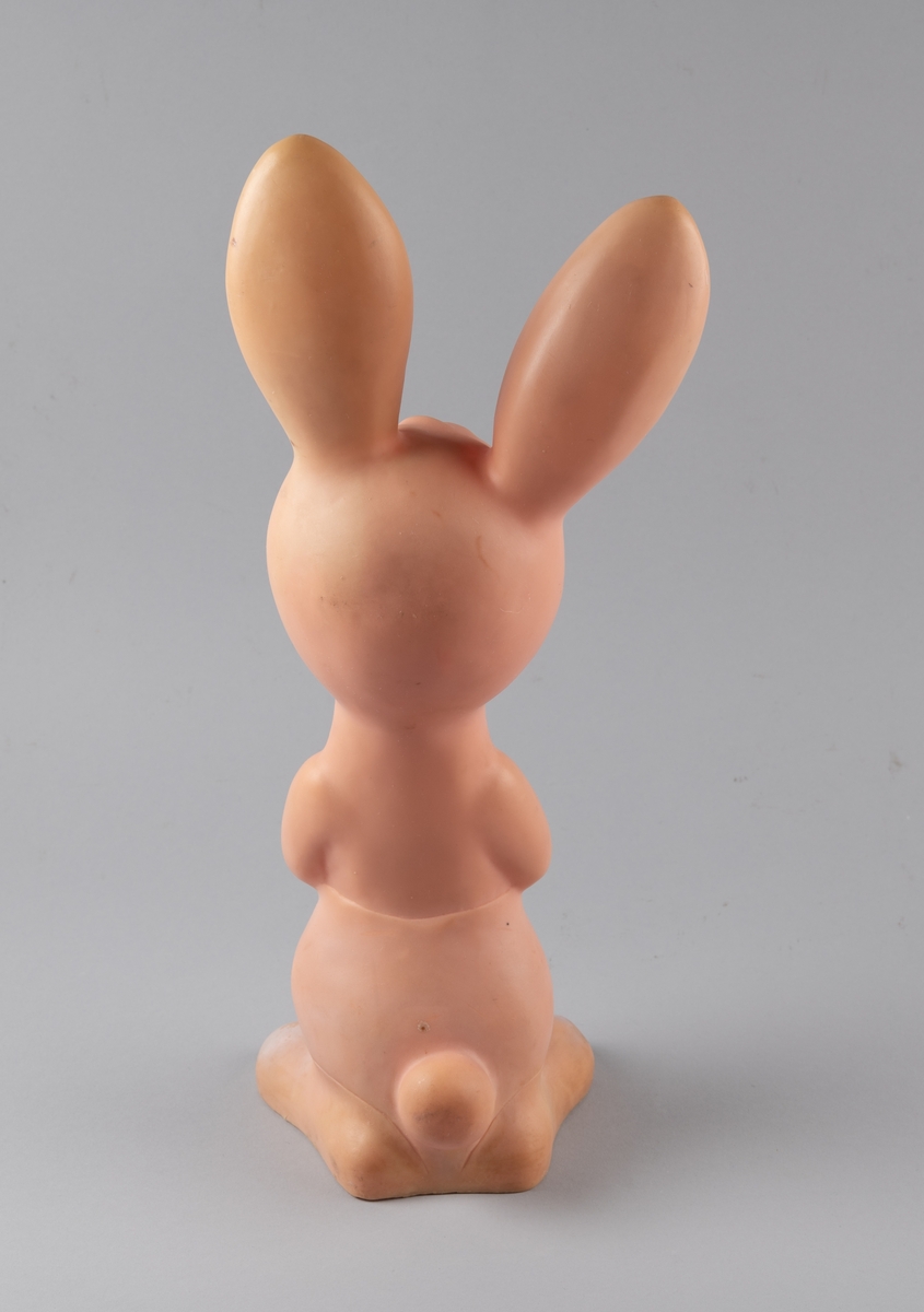 Leketøy av hardnet mykplast i form av en sittende hare. Den er rosa med blåe øyer, og ellers antydning til hvite og gule markeringer.
