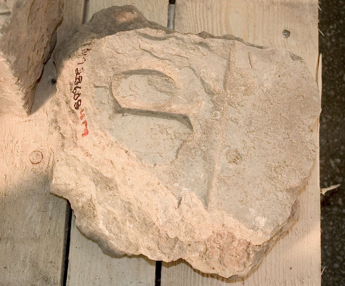 Fragment av gravhäll av kalksten, flagnande brottytor, med inhuggen bokstavsbård, bokstaven P.