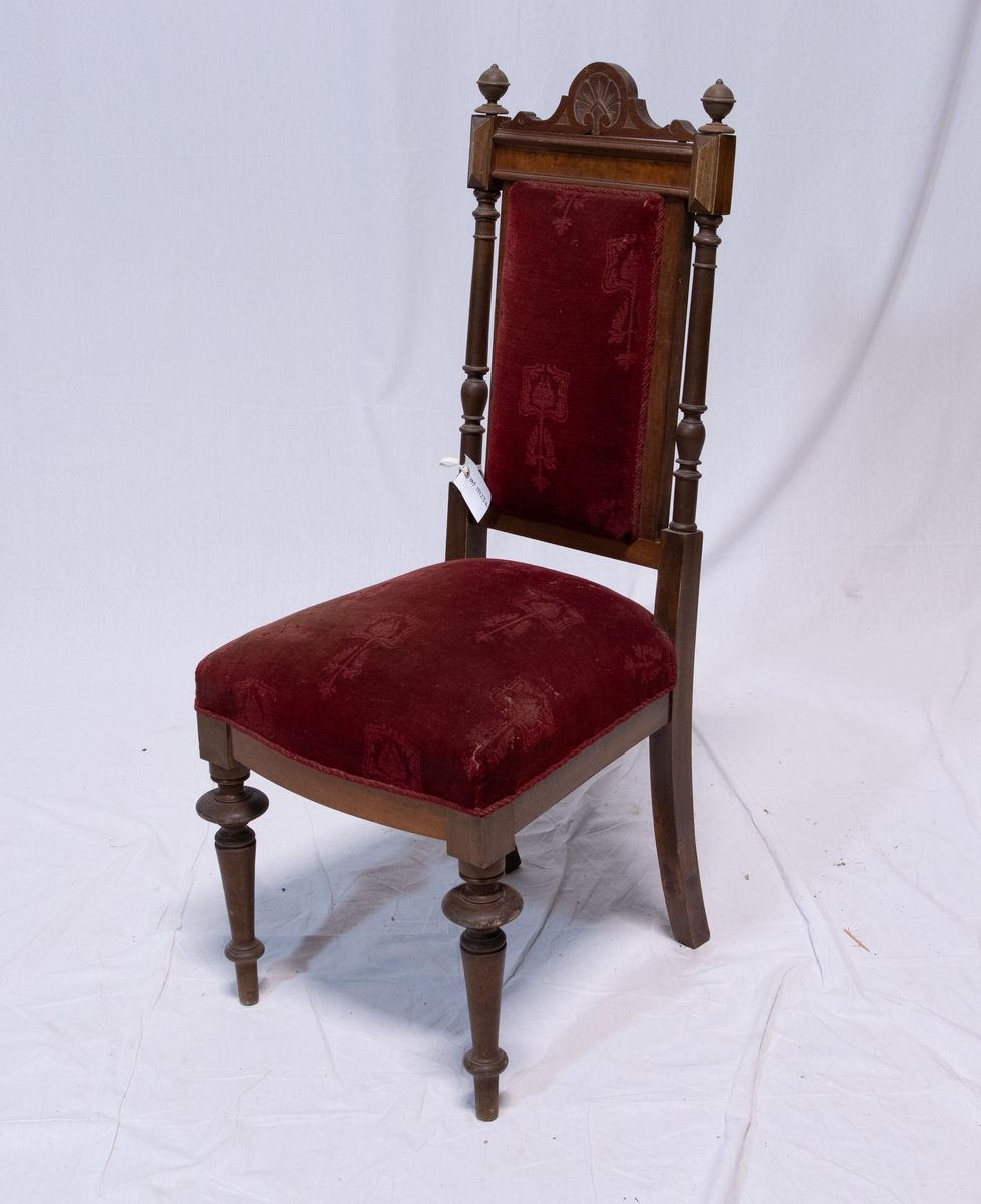 Stoler med høy rygg og dreide ben. Setetog stolryggen er polstret og trukket med rød fløyel. Stoffet har også et dekorativt mønster bestående av endring i tekstur. Treverket på stolryggen er dreid og utskåret i mønster ved toppen. To kuler kroner hver side av stolryggen.