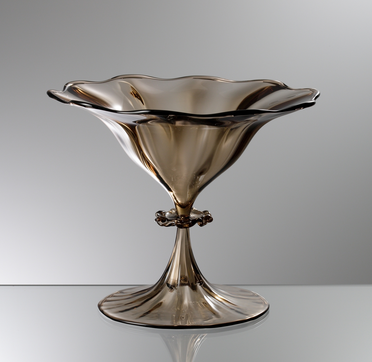 "Slottsglas" formgivet av Simon Gate till Göteborgsutställningen 1923. Friblåst och räfflat i ljusbrunt glas. Fot och kupa blåsta och drivna. Räfflat ben med en väl tilltagen knapp.