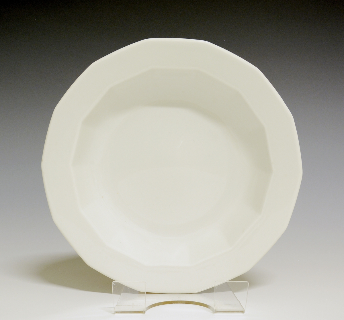 Mangekantet dyp tallerken av porselen med hvit glasur. 
Modell: Octavia, tegnet av Grete Rønning i 1977.
