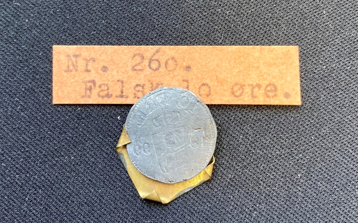 Falsk mynt; skal vistnok være en tiøre. Innlevert til Lademoens politistasjon i 1911. Nærmere opplysninger savnes.