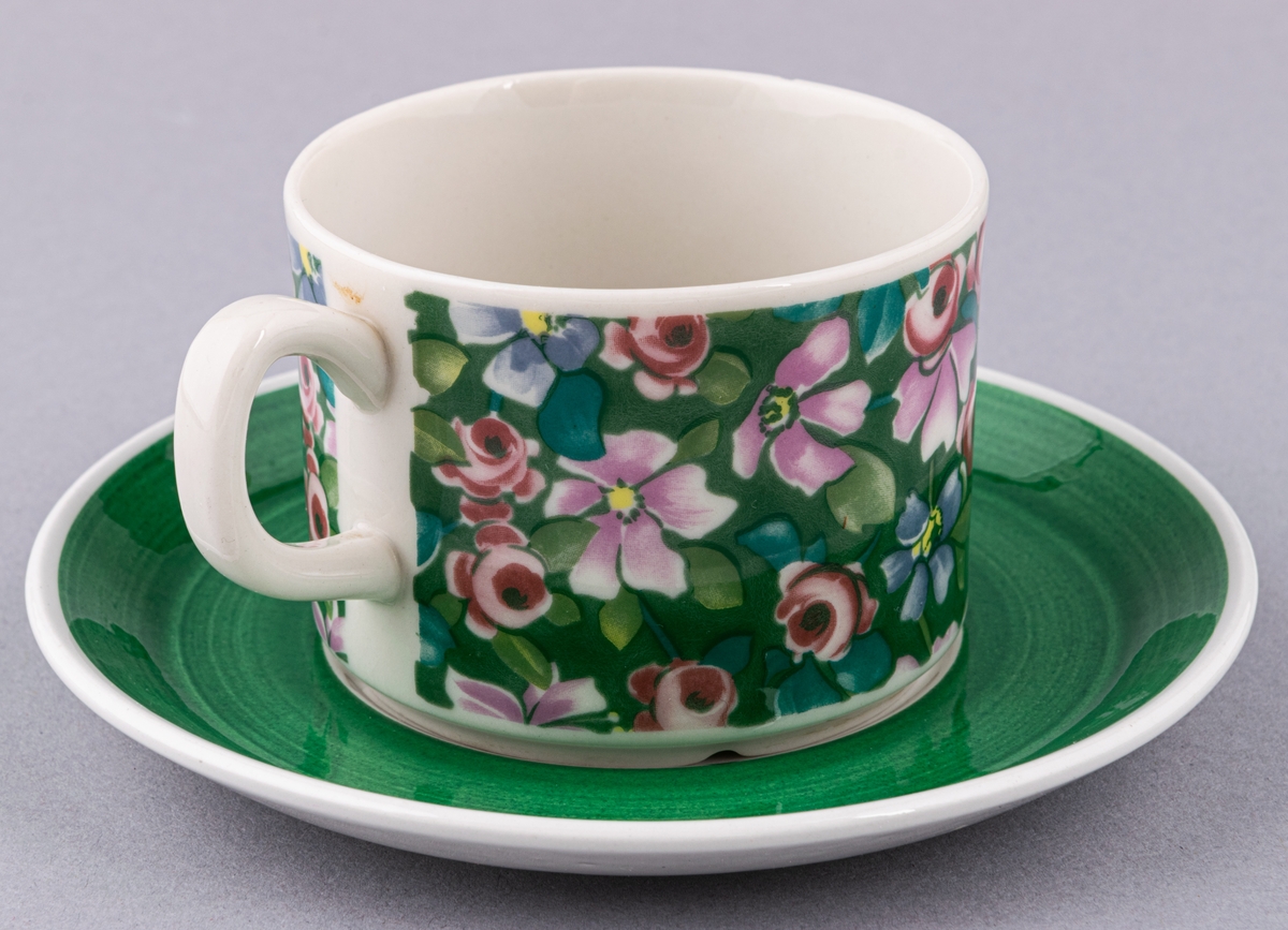 Kaffekopp med fat, i flintgods. Modell EH, dekor Flox (grön). Vit glasyr med grönt blommönster, grönt fat. Skapad av Helmer Ringström för Gefle Porslinsfabrik 1973.