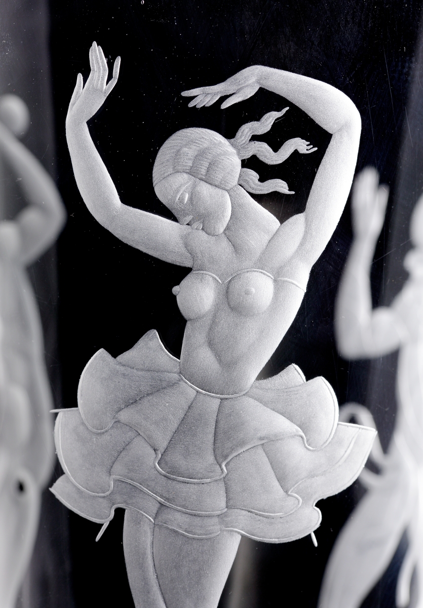 Formgiven av Vicke Lindstrand. Konande form med halvklotsformad fot. På kupan graverat figurmotiv föreställande en cirkusdansös, en harlekin och en akrobat.