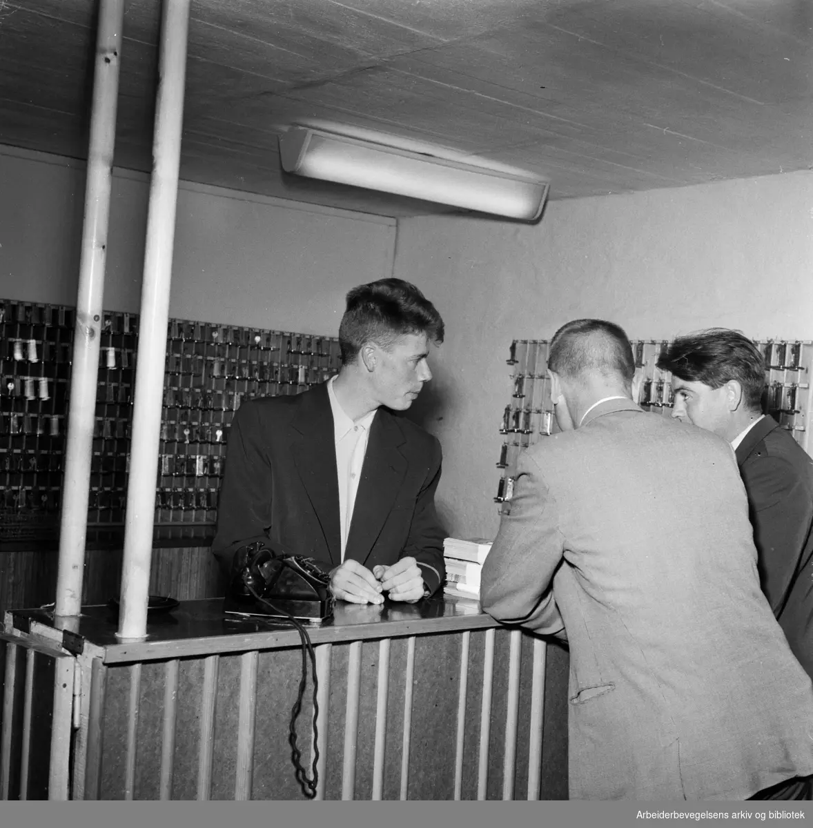Studentbyen på Sogn. Sommerhotellet. Provisorisk "Resepsjon B", som er innredet i en garasje. Bak disken står resepsjonsvakt Per Brøyn, som til daglig er stud.philol. Juni 1958