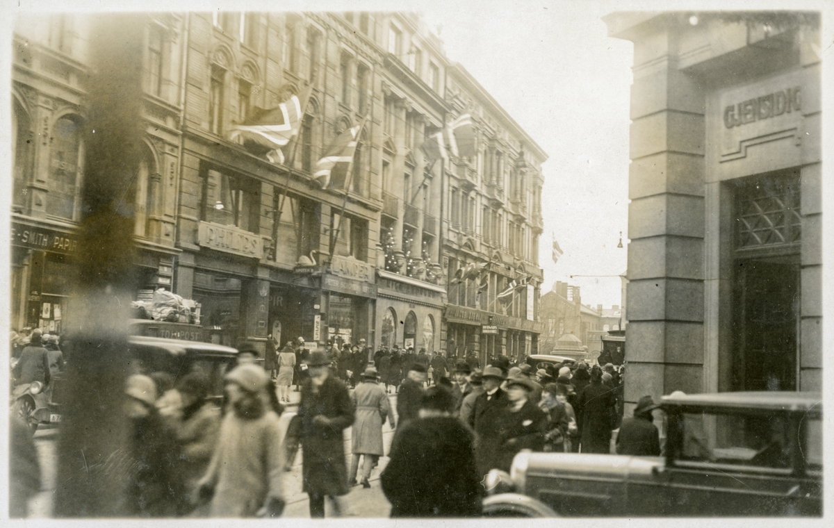 Karl Johans gate sett mot Stortinget med biler og fotgjengere, flagg på fasadene - Minnedagen for Roald Amundsen - 14. desember 1928.