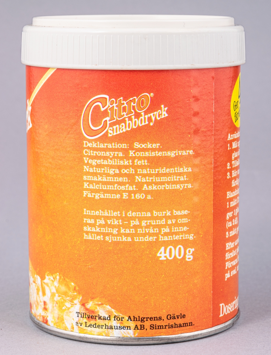 Cylinderformad plåtburk med plastlock, innehållet kvar. Orange pappersetikett, "Citro snabbdryck Apelsinsmak".