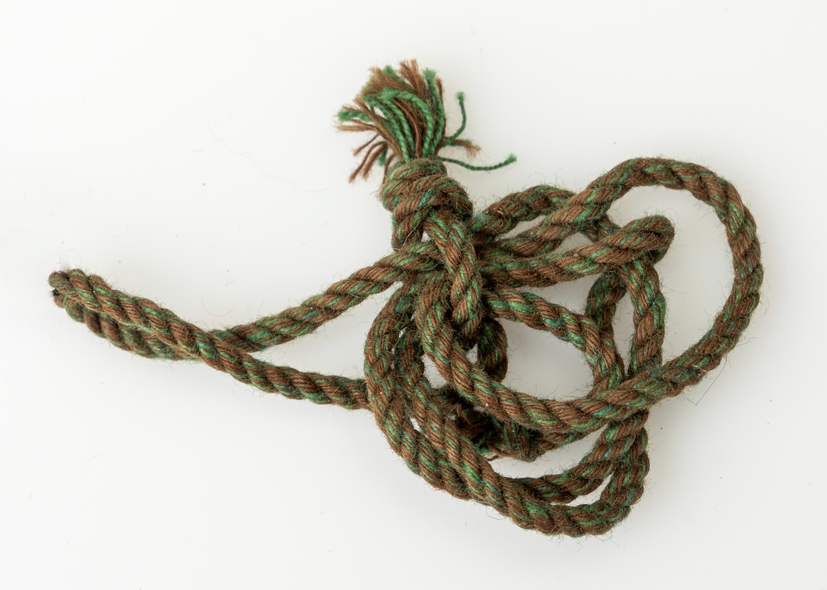 En snor tvunnet av grønt og brunt bomullsgarn. Den er tvunnet av to tråder og er knyttet i hver ende.
