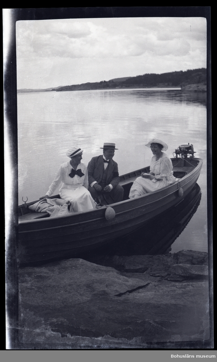Tre person sittandes i en båt vid en klipphäll.