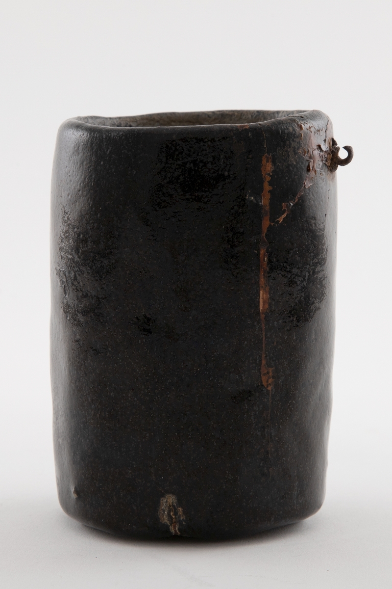 Vase i glasert keramikk. Vasen har ujevn flate, mulig håndformet, og er glasert i sort. Uglasert på innsiden. I øvre del, på utsiden, finnes en liten metallring, antakelig til oppheng.