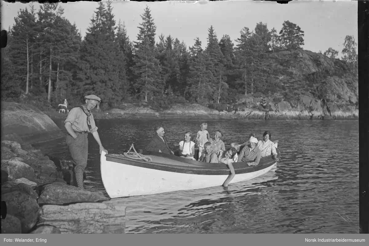 Ungdom stående på land og holder båt med mennesker sittende i. På land i bakgrunnen ståe en kvinne med en ku.