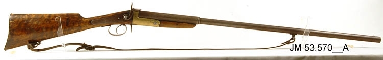 Hagelbössa, en så kallad stiftantändare, även kallad "Hovslättsbössan", tillverkad omkring år 1900. Avsett för stiftantändning. Piplängd 796 mm. Kaliber 16 mm, hyllslängd 6 cm. Tillverkningsnummer (vapennummer) saknas, men om pipan fälls ner syns numret 26 stämplat i metallen. Försedd med vapenrem av läder. Orört originalvapen. 

På kolven är inskuret mönster vid handgreppet och årtalet "1912" Detta är gjort av den tidigare ägaren Jesper Gustavsson. Årtalet avser det år vapnet kom till familjen Gustavsson.

Tillhörande Deklarationsbevis nr 139, år 1934 för målaren Verner Gustav Oskar Gustavsson, Åsa Lilla, Sandseryds socken.

Tillbehör:
1. Patronutdragare (ringformad)
2. Patronutdragare (nyckelformad)
3. Patroner, 15 st
4. Rengöringsdon i snöre
5. Ask med lösa hagel
6. Krok (dubbelkrok/hatthylla)
