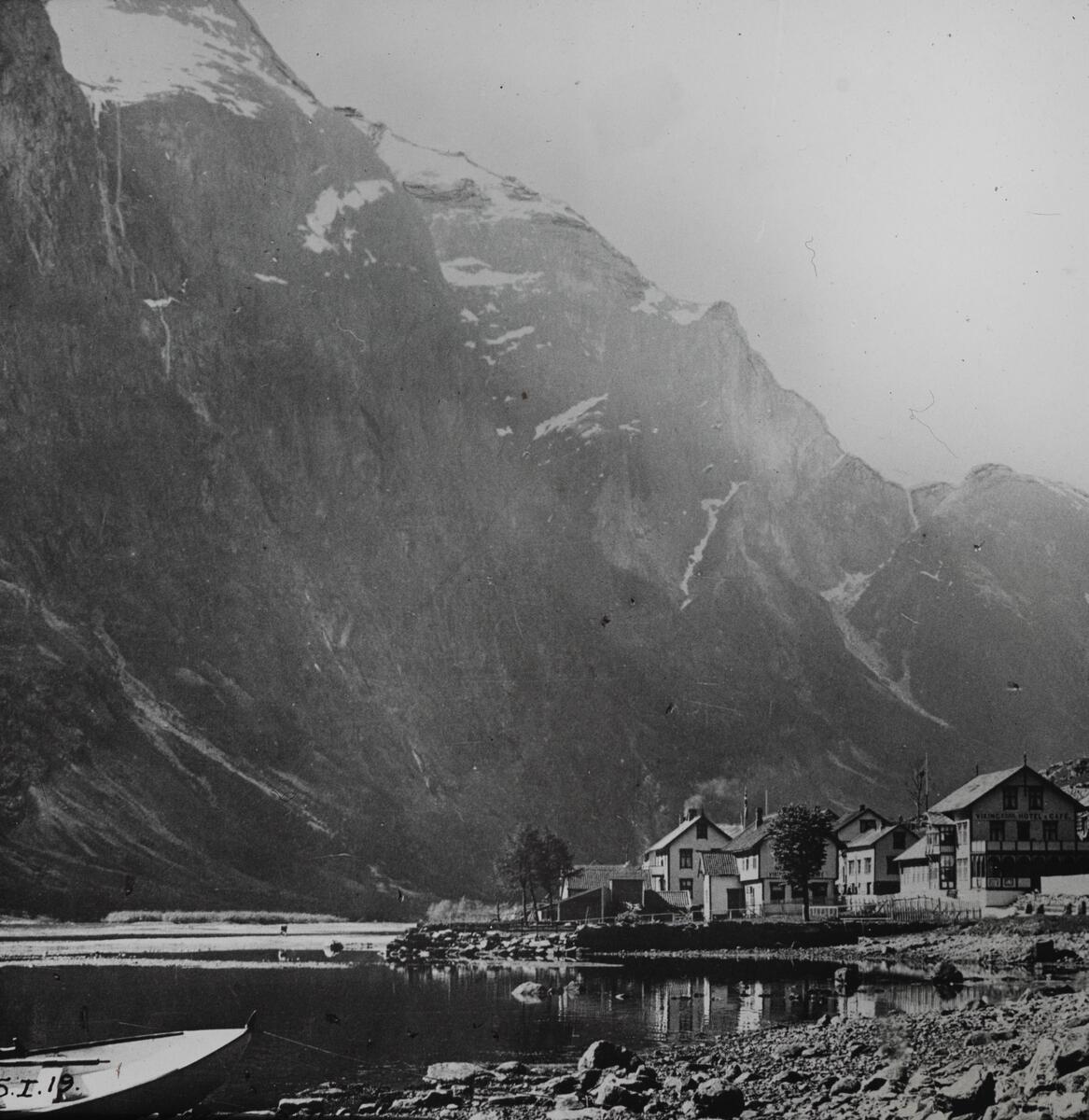 Dias. En gruppe trehus i sveisterstil ligger på et nes i en fjord omgitt av bratte fjell.