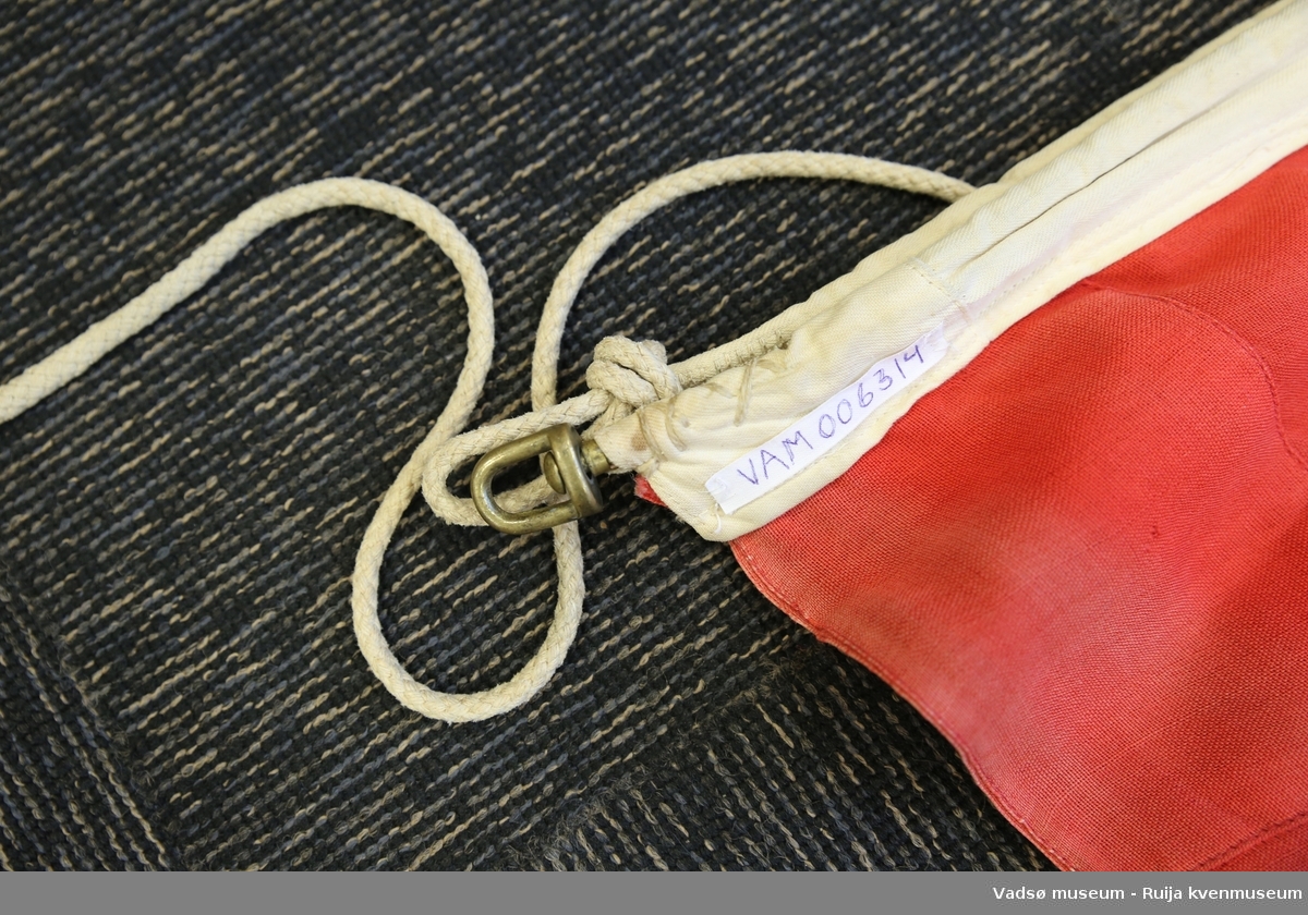 Norsk flagg i vevd materiale, antatt syntetisk. Løpegang og snor av bomullstoff. Flagget har maskinsydd søm, hvitt og rødt er brukt.