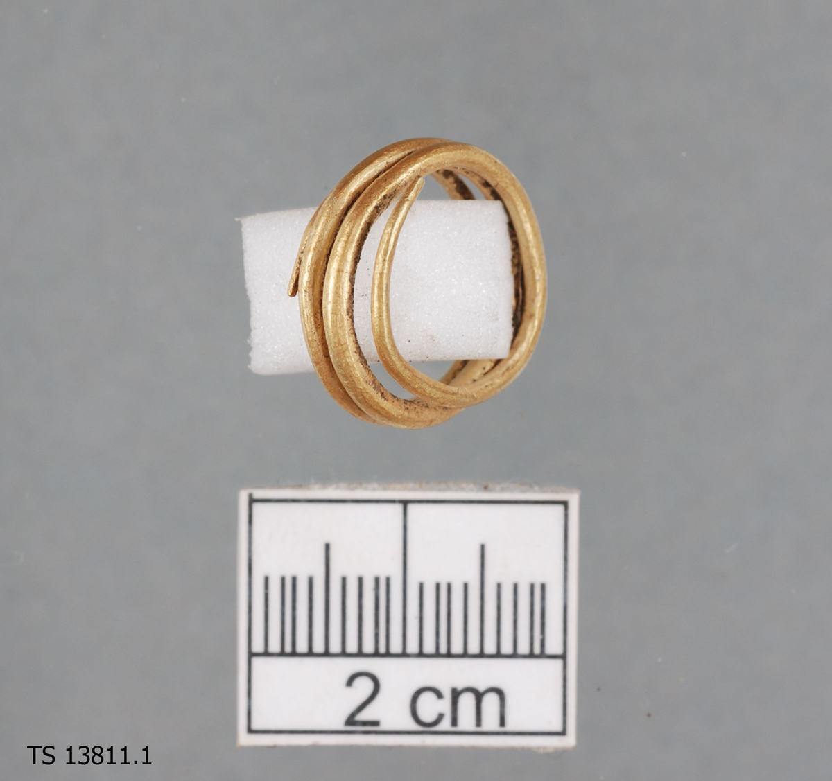 Betalingsring av gull, 1 stk., trolig fra eldre jernalder, likner Rygh 1885 figur 183. Ringen har tre hele omdreininger, som delvis ligger kant i kant. Gulltråden har et tilnærmet rundt tverrsnitt. Ringen er tykkest midt på spiralen og avsmalner i hver ende. Endene er
spisse. Ringen er 1,8 cm i diameter, største høyde 0,7 cm og største tykkelse på tråden er 0,15 cm. Vekt 3,94 gram. 