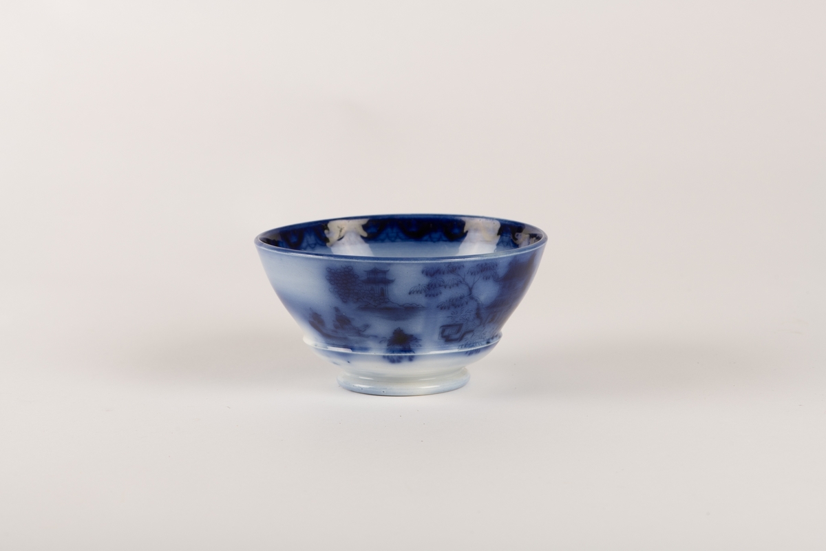 En hvit skål med ulike geometriske- og blomstermotiver malt i blått.