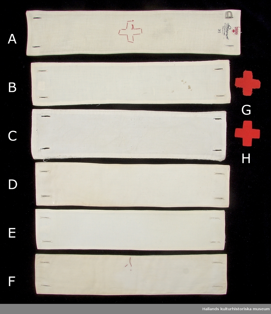 Samling av armbindlar tillhörande sjuksköterska.

A: Armbindel av fodrad vit bomullsväv. Manglad och stärkt. Armbindeln bär Röda Korsets symbol i rött bomullstyg. Hålls ihop med två manschettknappar, varav den ena saknas. På avigsidan finns en etikett med röd text: "2809" åtföljt av ett rött kors. Bredvid etiketten en tillverkarstämpel i svart bläck (se foto)
Längd: 375 mm. Höjd: 77 mm.

B: Armbindel av fodrad vit bomullsväv. Manglad och stärkt. Två förstärkta hål på vardera kortsida för manschettknappar. På avigsidan finns en etikett med röd text: "2809" åtföljt av ett rött kors. Bredvid etiketten en tillverkarstämpel i svart bläck (se foto), samt "T-35".
Längd: 350 mm. Höjd: 74 mm.

C: Armbindel av fodrad vit bomullsväv. Manglad och stärkt. Två knapphål på vardera kortsida.. Märkt med bläck längs ena kortsidan: "A.M. 4.A" samt en figur som består av tecknen "VII" omgärdat av en överstruken ring. 
Längd: 345 mm. Höjd: 85 mm.

D: Armbindel av fodrad vit bomullsväv. Manglad och stärkt. Två knapphål på vardera kortsida. Längs en av kortsidorna finns en tillverkarstämpel samt texten: "T 34". 
Längd: 345 mm. Höjd 77 mm.

E: Armbindel av fodrad vit bomullsväv. Manglad och stärkt. Två knapphål på vardera kortsida. På en av kortsidorna en svårtydd tillverkarstämpel med svart bläck; ovanför stämpel sitter en etikett med röd text: "BS 144". 
Längd: 340 mm. Höjd: 73 mm.

F: Armbindel av fodrad vit bomullsväv. Manglad och stärkt. Två knapphål på vardera kortsida. I mitten av armbandet finns rester av röd tråd vilket troligtvis är ett spår efter ett tygmärke. På en av avigsidorna en etikett med röd text: "2809" åtföljt av ett rött kors. Under etiketten en tillverkarstämpel i svart bläck (se foto), samt "T 34". 
Längd: 345. Höjd: 72 mm.

G: Tygmärke av röd bomullsväv föreställande röda korsets symbol. Tygmärket saknar sömmar längs kanterna och är därmed fransigt - ofärdigställt. Tygmärket skall fästas i armbindel.
Längd: 45 mm. Höjd 45 mm.

H: Tygmärke av röd bomullsväv föreställande röda korsets symbol. Sömmar längs kanterna. Tygmärket skall fästas i armbindel.
Längd: 45 mm. Höjd 45 mm.