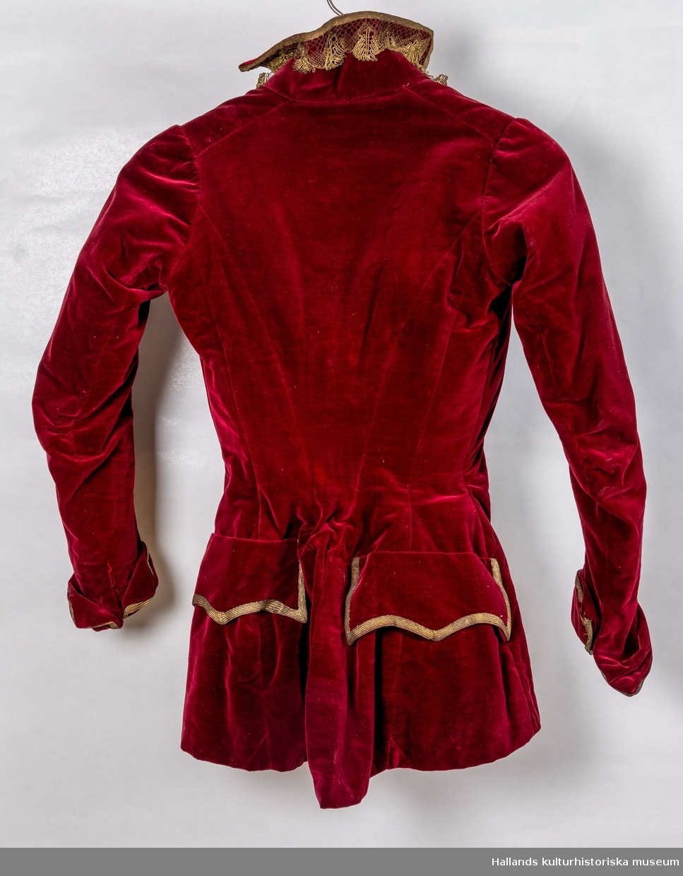 Maskeraddräkt av vinröd sammet bestående av lång kjol, knäbyxor och jacka.
