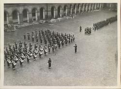 Korps og uniformerte menn stående på brosteinslagt plass for