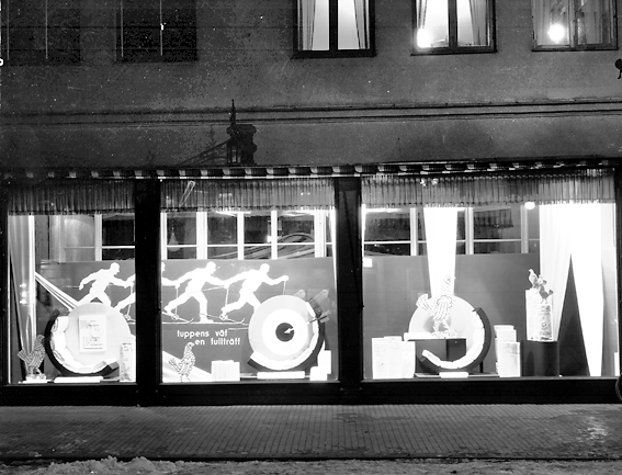 Bild tagen på kvällen i skyltfönstren hos Ekelöf & Svensson AB.
1872 etablerade fröknarna Hilda Ekelöf och Carolina Svensson en detaljaffär i manufaktur. Vacklande hälsa gjorde att firman 1897  överläts till Wilh. Welin som skapade nya avdelningar, till exempel flaggtillverkningen (1900) och en syatelje för klänningar (1905) samt en modeaffär (1914) där bland annat Josefin Baker gick modell.  Sommaren 1999 lades verksamheten ner på grund av olönsamhet.
Källa: Nyblom-Svanqvist, Näringsliv i Värmland, 1945 och Värmlands Folkblad.