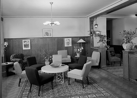 Interiör från hotellet med fåtöljer, bord, lampor och blommor.
Fotografens ant: Turisthotellet Edsgatan.