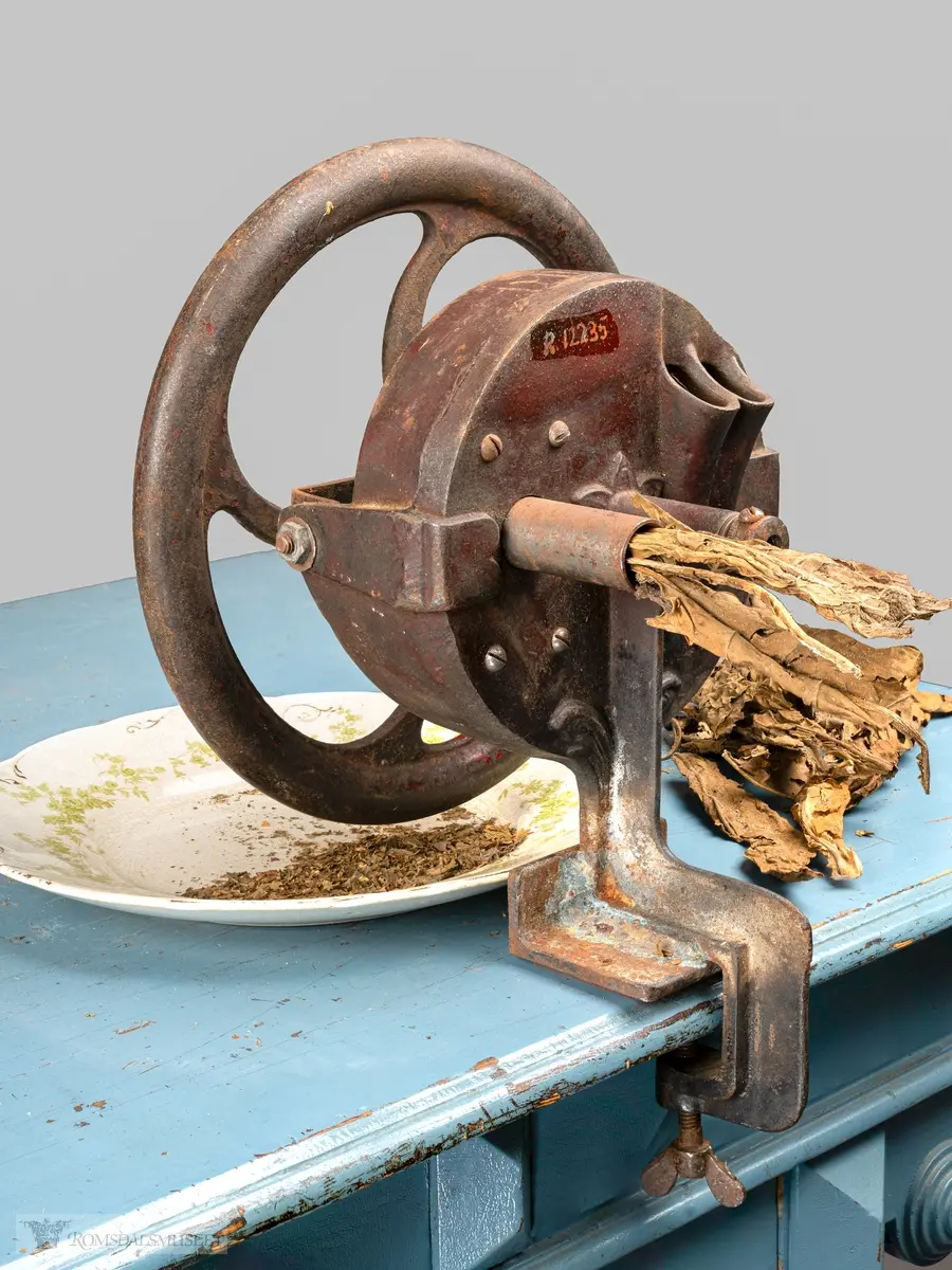 Bordfeste med skrue. Stort hjul med sveivehåndtak på hjulets ytterside, nav med kniver som går rundt når man sveiver.  opprinnelig bønnesnittemaskin som har blitt modifsisert for kutting av hjemmedyrket tobakk.
