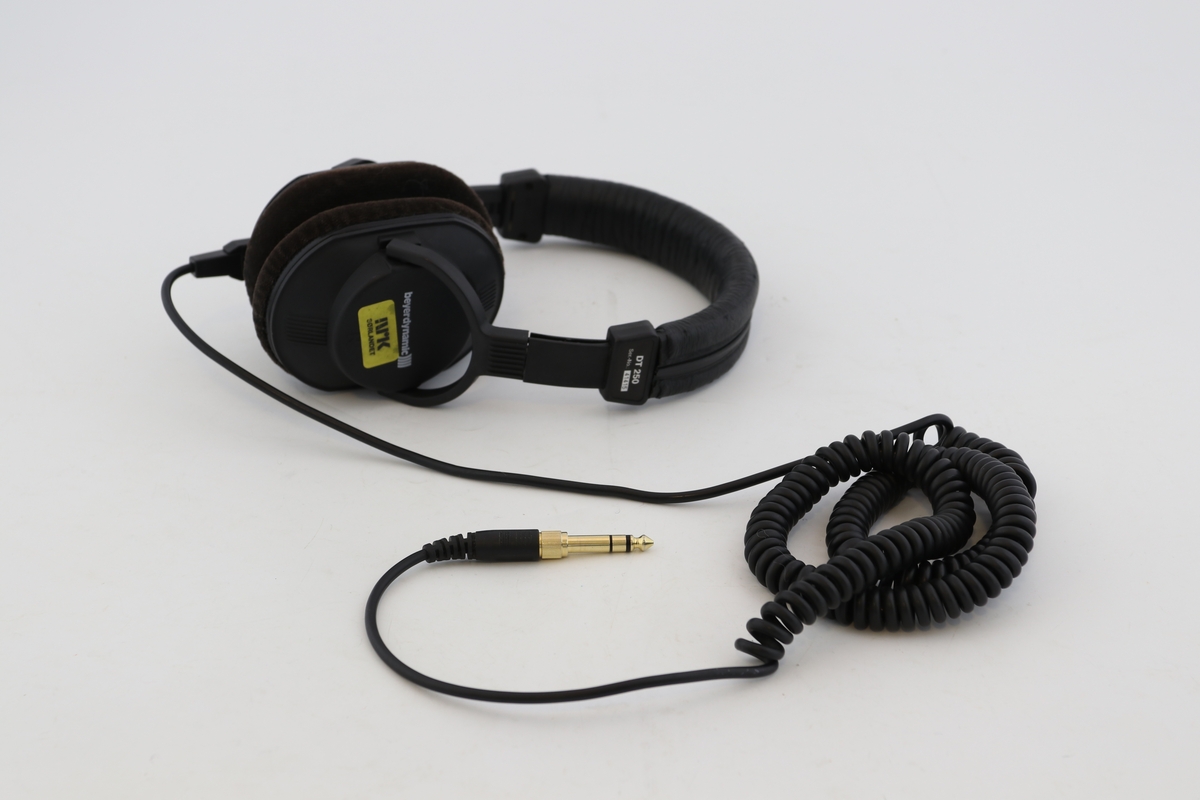 Svarte hodetelefoner med spiralledning. Fløyelsstoff på øreklokkene mot brukeres ører.