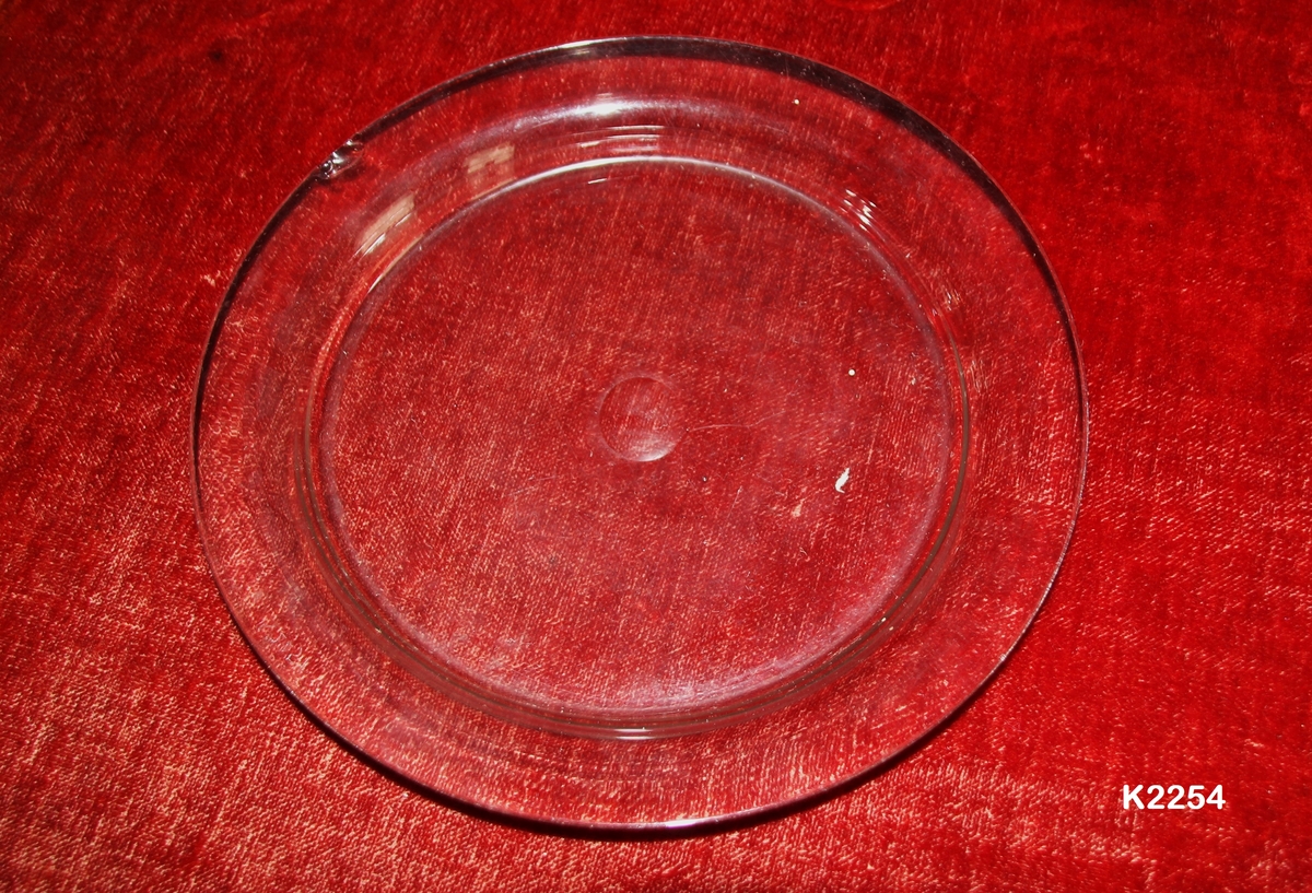 Glassfat (til osteklokke?) 
Glass, klart, blåst.
Stort flatt speil med avklipningen slipt som en sirkel. Utoverbuet brem.